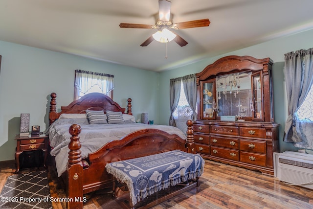 bedroom featuring multiple windows, a ceiling fan, an AC wall unit, and wood finished floors