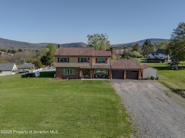 traditional-style house with an attached garage, a front lawn, a mountain view, and driveway