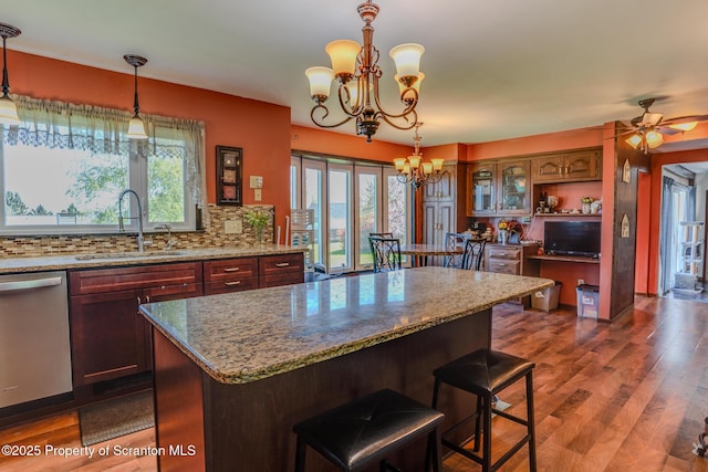 kitchen with dark wood-style flooring, a sink, decorative backsplash, stainless steel dishwasher, and a kitchen island