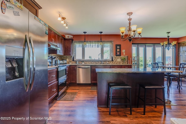 kitchen with an inviting chandelier, tasteful backsplash, a kitchen island, and stainless steel appliances