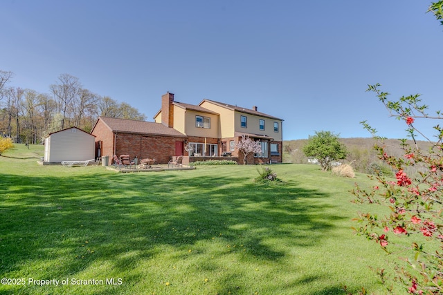 rear view of property with a lawn, brick siding, a chimney, and an outdoor structure