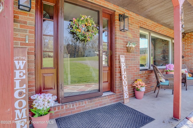 view of exterior entry with a porch and brick siding