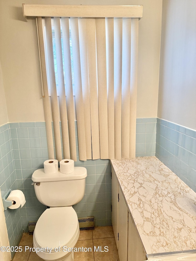 half bath with toilet, a wainscoted wall, tile patterned floors, vanity, and tile walls