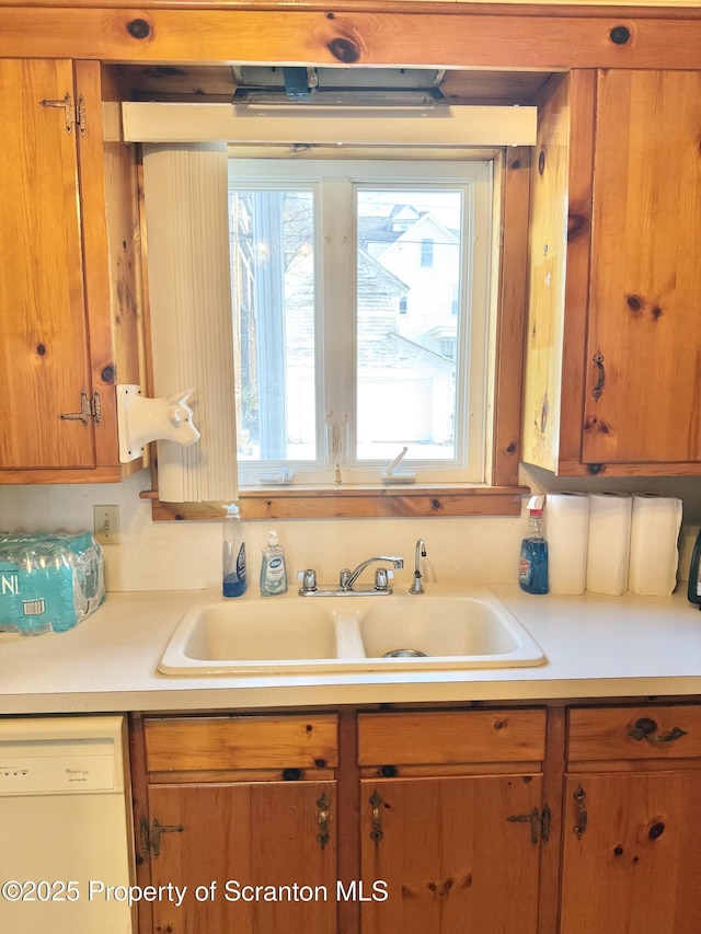 kitchen with dishwasher, light countertops, brown cabinetry, and a sink