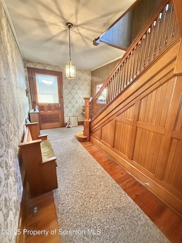 unfurnished living room featuring ornamental molding, stairway, wood finished floors, and wallpapered walls