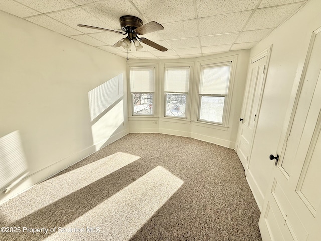 carpeted empty room featuring a drop ceiling, a ceiling fan, and baseboards