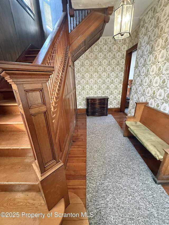 stairs with wood finished floors, crown molding, baseboards, and wallpapered walls