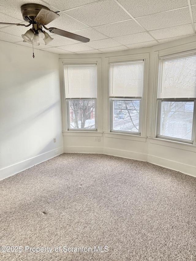 carpeted empty room featuring ceiling fan, baseboards, and a drop ceiling