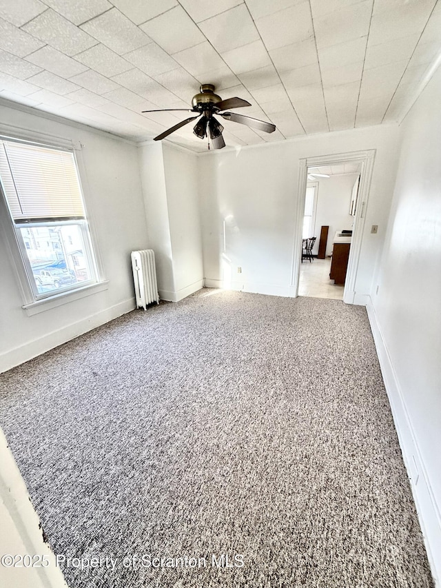 empty room with carpet, radiator heating unit, baseboards, and ceiling fan