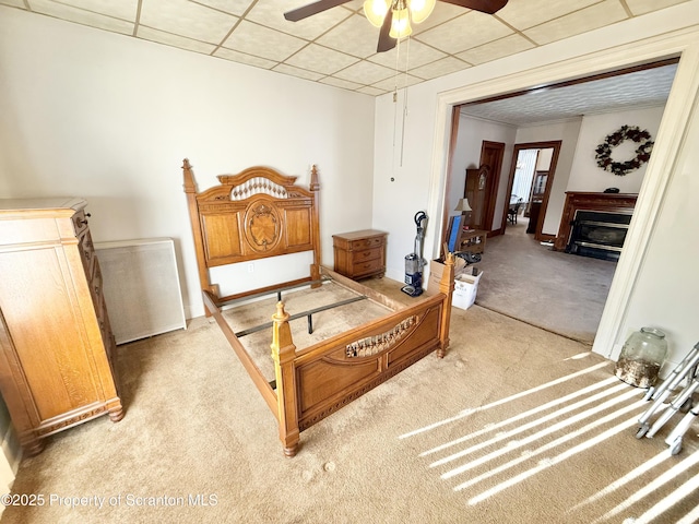 bedroom featuring light carpet, ceiling fan, a fireplace, and a drop ceiling