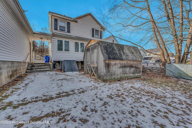 snow covered rear of property featuring a shed