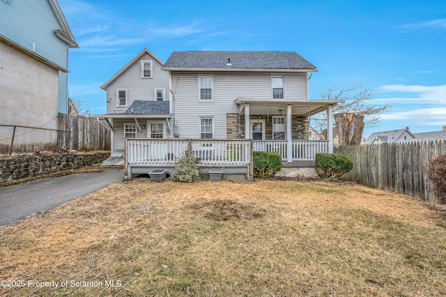 back of property featuring fence private yard, a lawn, stone siding, and roof with shingles