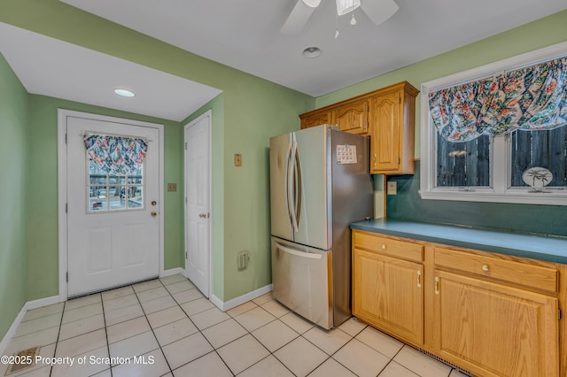 kitchen featuring brown cabinetry, ceiling fan, baseboards, freestanding refrigerator, and light tile patterned flooring