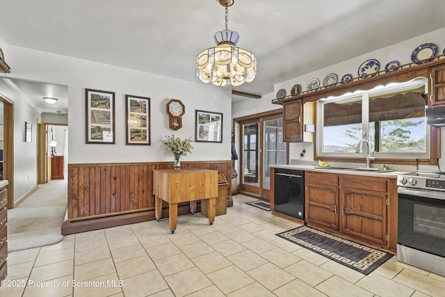 kitchen with black dishwasher, stainless steel electric range oven, light countertops, wainscoting, and a sink