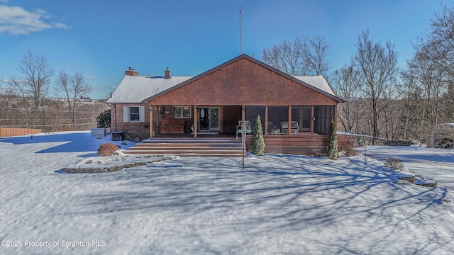 snow covered property featuring a chimney and a sunroom