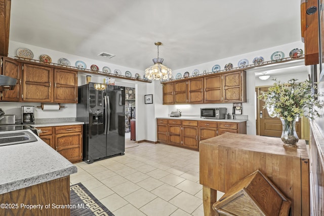 kitchen with visible vents, stainless steel microwave, black refrigerator with ice dispenser, light countertops, and pendant lighting