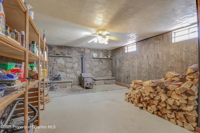 basement featuring a ceiling fan, a wood stove, and wooden walls