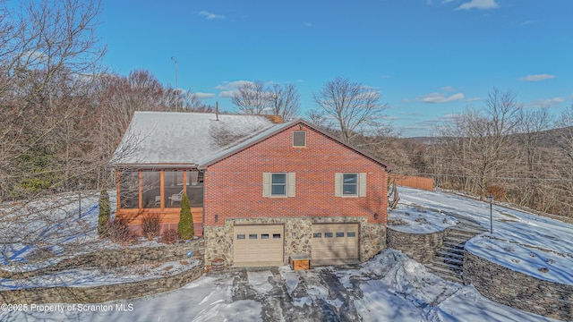 view of snow covered exterior featuring a garage, stone siding, and brick siding