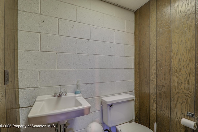 bathroom featuring concrete block wall, toilet, and a sink