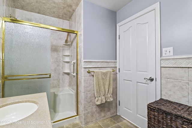 bathroom with a stall shower, a wainscoted wall, tile walls, and vanity