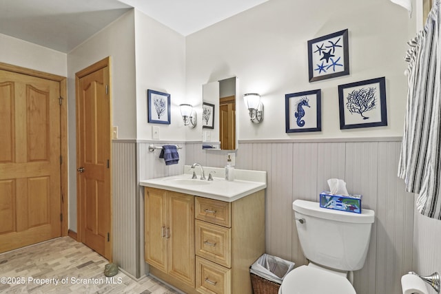 half bathroom with a wainscoted wall, wood finished floors, vanity, and toilet