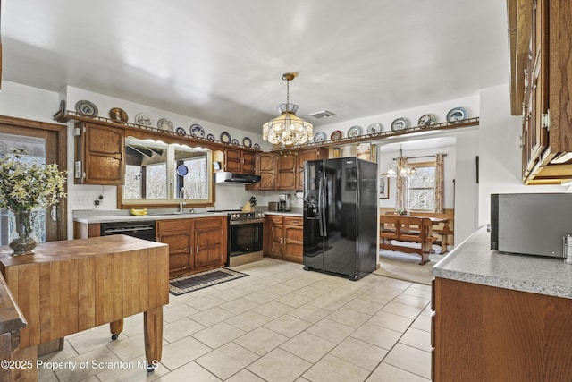 kitchen with decorative light fixtures, a notable chandelier, light countertops, under cabinet range hood, and black appliances