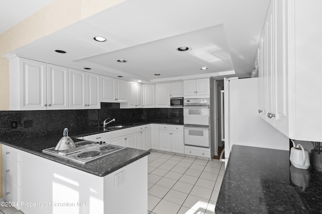 kitchen with a raised ceiling, stovetop, light tile patterned floors, double oven, and white cabinets