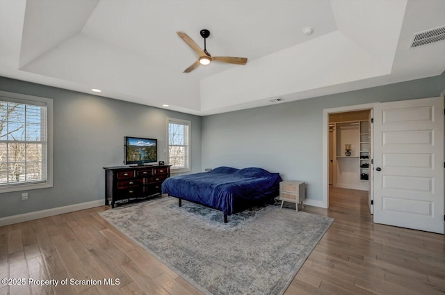 bedroom featuring wood finished floors, a raised ceiling, visible vents, and baseboards