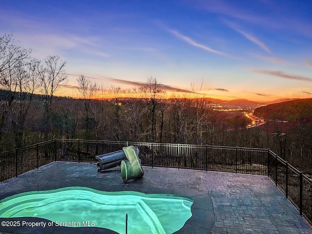 pool at dusk with a fenced in pool, a patio area, and a view of trees