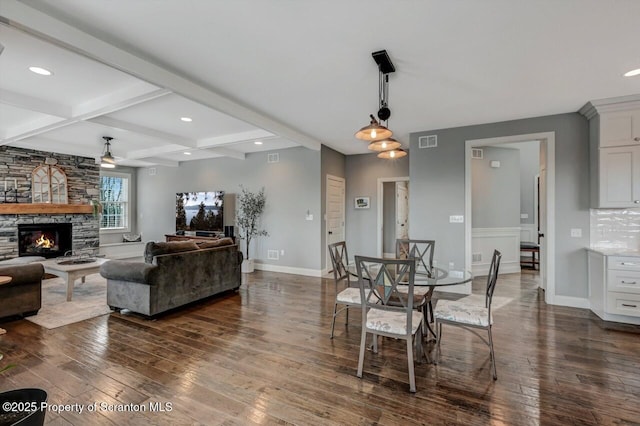 living area featuring baseboards, visible vents, dark wood-style flooring, a fireplace, and beam ceiling