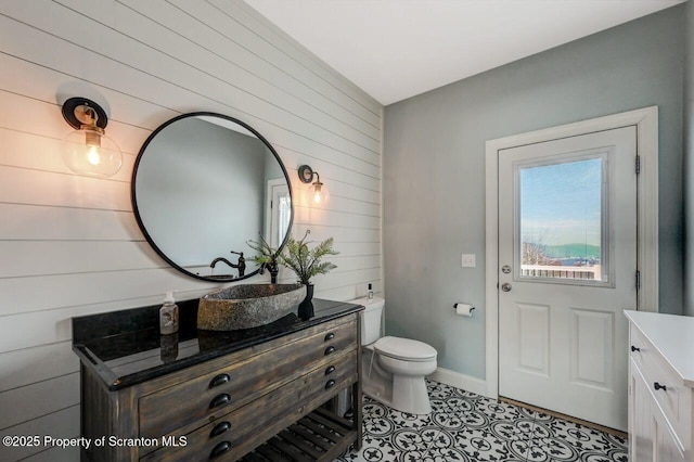 bathroom with toilet, wood walls, vanity, baseboards, and tile patterned floors