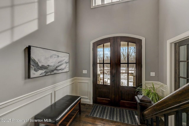 entryway featuring arched walkways, french doors, a wainscoted wall, and wood finished floors