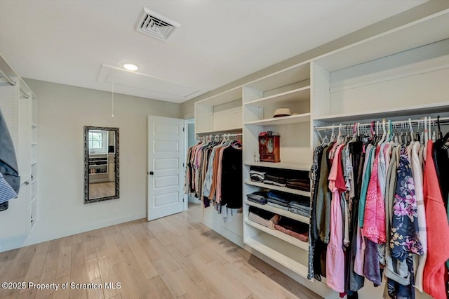 spacious closet with light wood finished floors, visible vents, and attic access