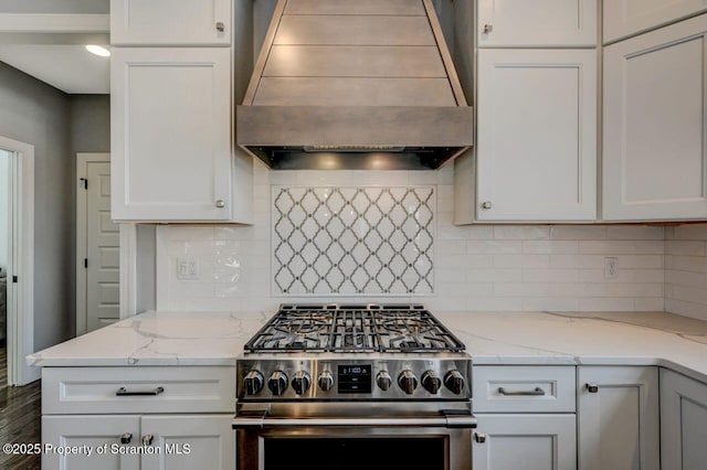 kitchen featuring stainless steel range, decorative backsplash, white cabinets, light stone countertops, and premium range hood