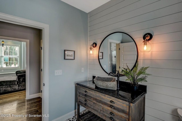 bathroom featuring wooden walls, vanity, baseboards, and wood finished floors