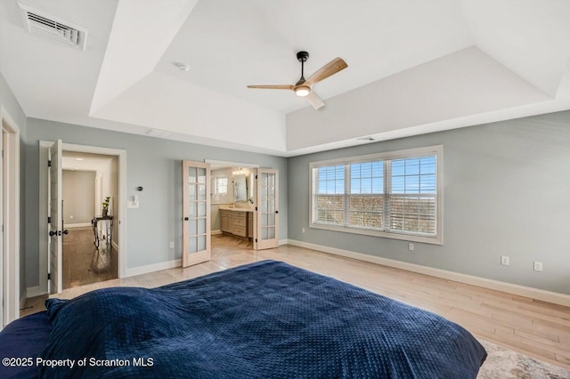 bedroom featuring baseboards, visible vents, a tray ceiling, and wood finished floors