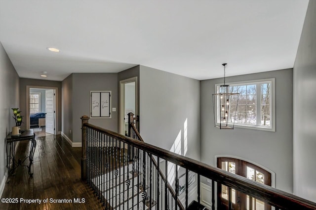 hall featuring baseboards, a chandelier, dark wood-style flooring, and an upstairs landing