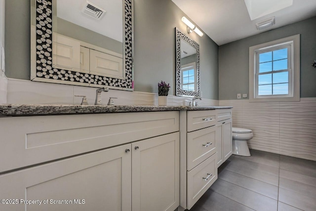 full bath featuring toilet, double vanity, visible vents, and tile walls