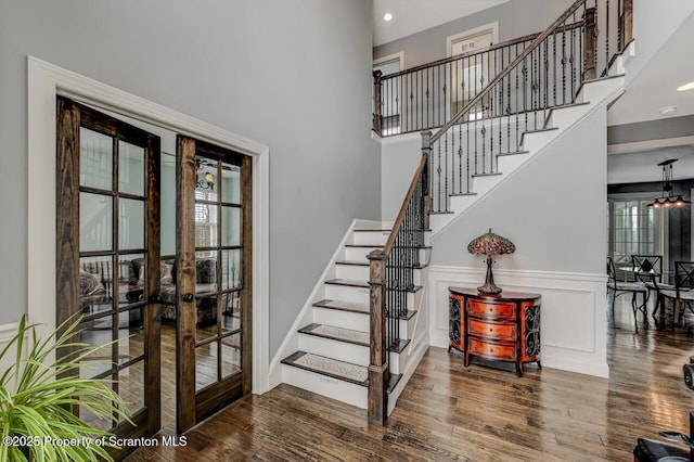 staircase featuring a decorative wall, a high ceiling, wood finished floors, french doors, and wainscoting