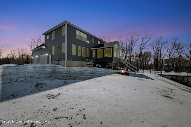 view of snow covered exterior with driveway, stairway, fence, and a sunroom