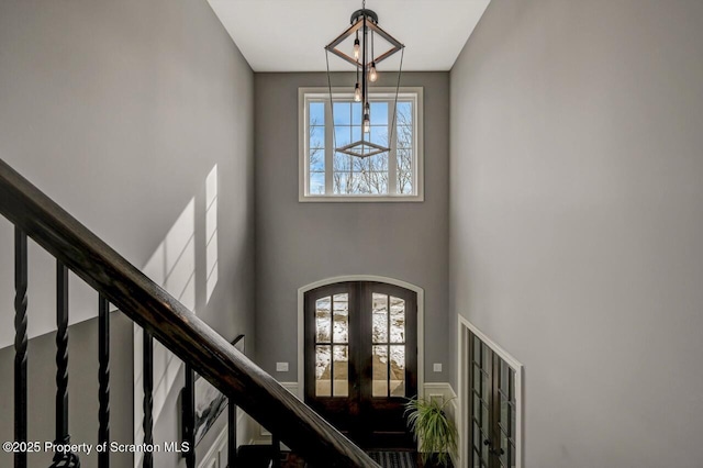 entrance foyer with a high ceiling, stairway, arched walkways, and french doors