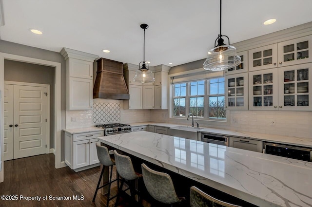 kitchen featuring dark wood finished floors, custom range hood, glass insert cabinets, pendant lighting, and a sink