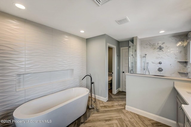 full bath with toilet, a tile shower, vanity, a freestanding tub, and recessed lighting