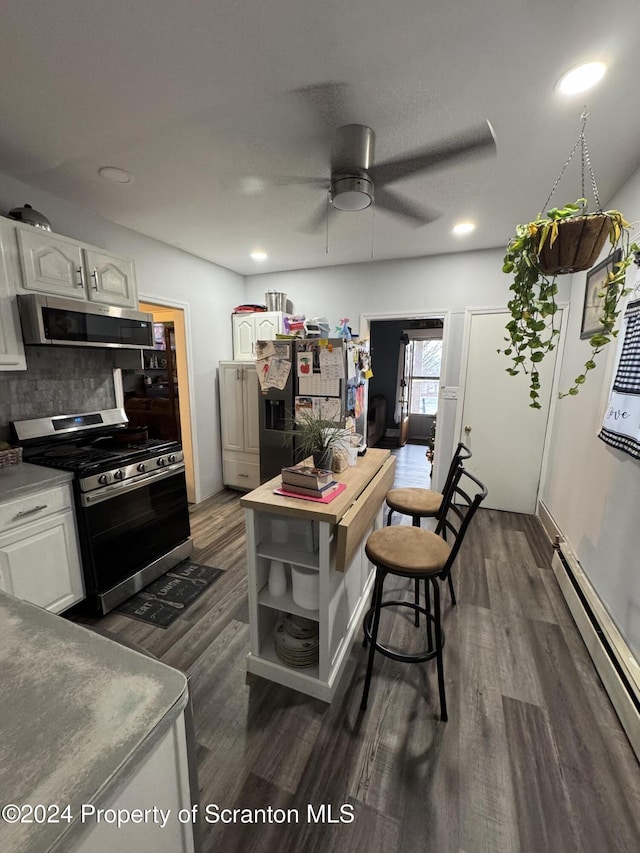 kitchen featuring white cabinetry, dark hardwood / wood-style flooring, a baseboard heating unit, decorative backsplash, and appliances with stainless steel finishes