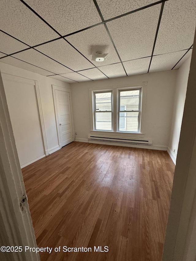 unfurnished room with a baseboard radiator, a paneled ceiling, baseboards, and wood finished floors