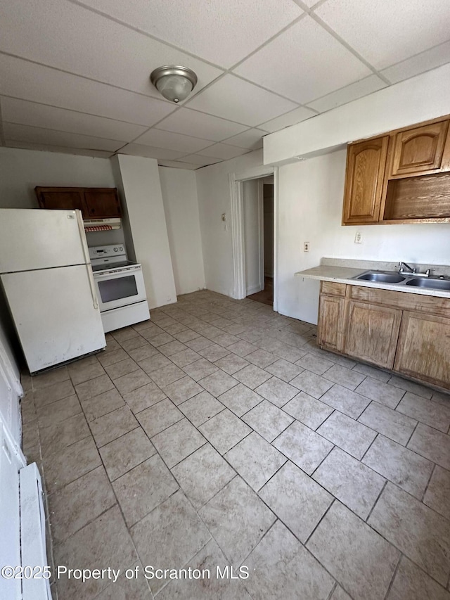 kitchen featuring white appliances, light tile patterned floors, a sink, a paneled ceiling, and brown cabinets