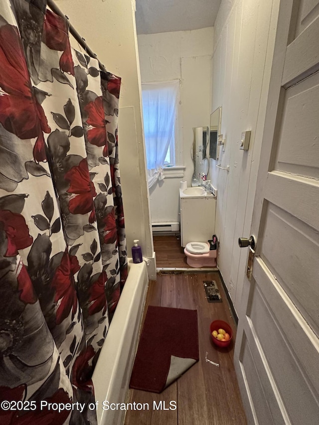 bathroom featuring a sink, toilet, a baseboard heating unit, and wood finished floors