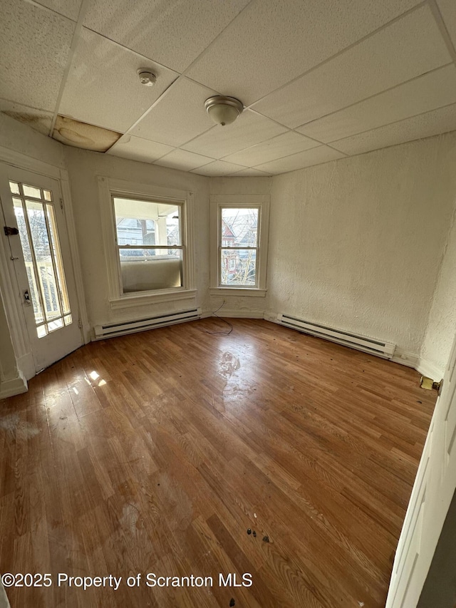 unfurnished room featuring a drop ceiling, wood finished floors, a textured wall, and a baseboard radiator