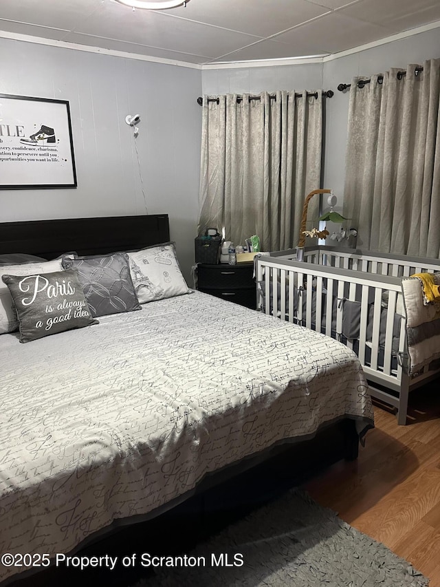 bedroom with ornamental molding and wood finished floors