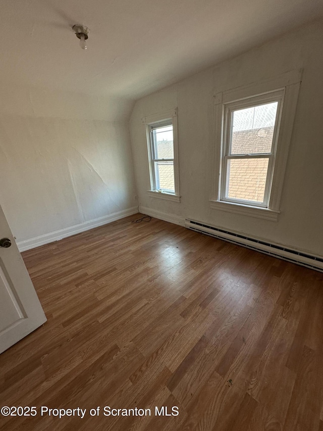 unfurnished room with a baseboard heating unit, vaulted ceiling, wood finished floors, and baseboards